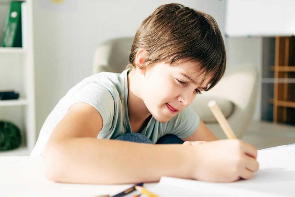 kid with dyslexia drawing with pencil and sitting at table