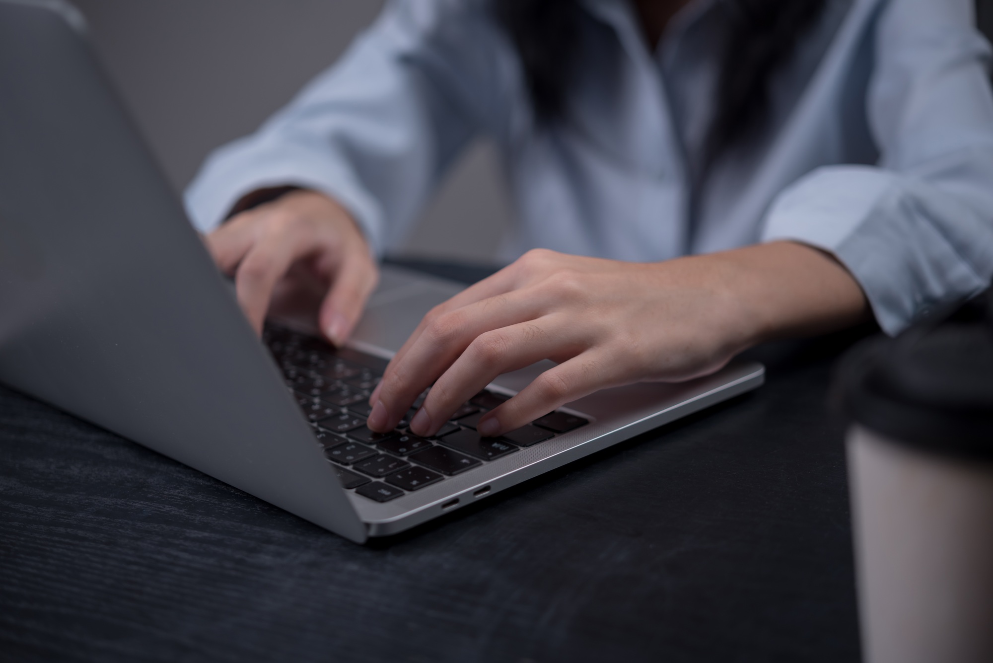 Close-up of hands typing on laptop keyboard at dark wooden desk