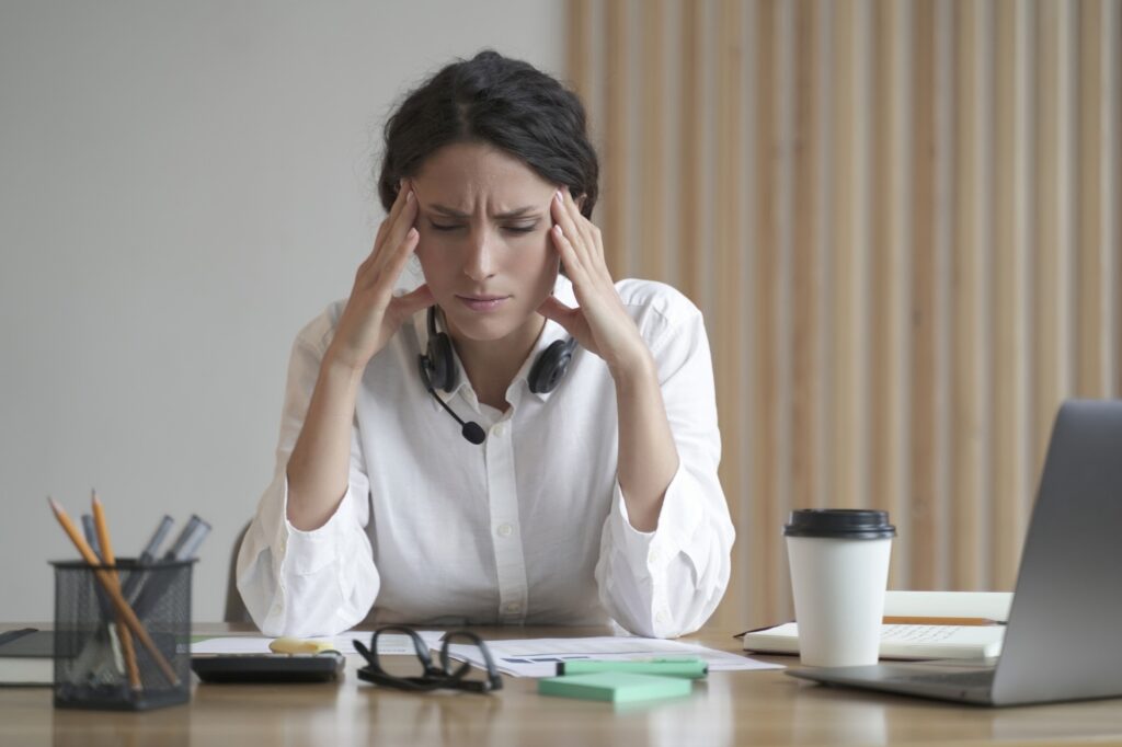 Stressed female professional with headache at work, feeling exhausted