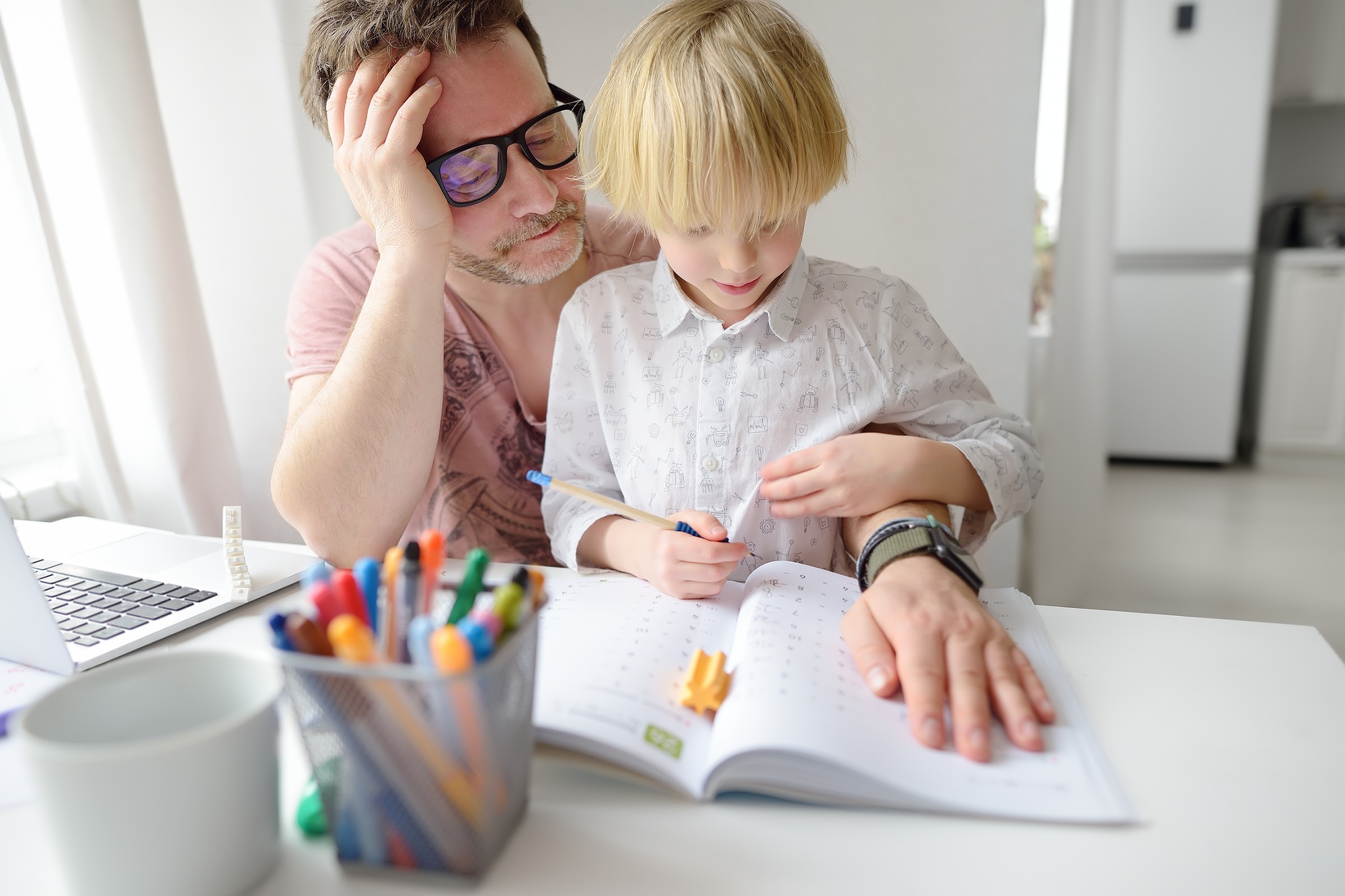 Tired father helping school boy with ADHD do his homework at home.