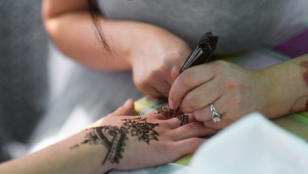 Artist applying henna tattoo on women hands