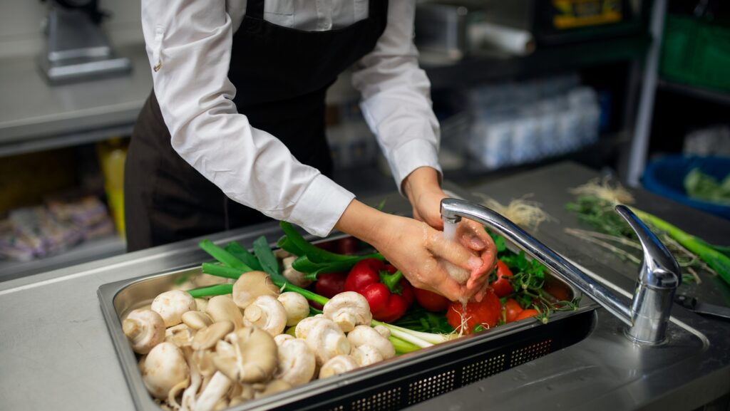 Close-up of cook washing vegetables in sink in commercial kitchen