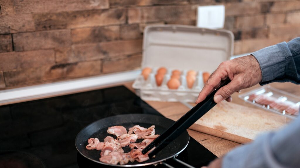 Senior man frying bacon.