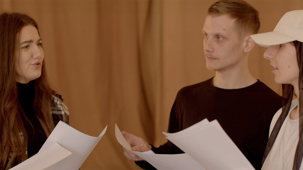 Students hold scripts in hands discussing literary readings, reading roles.