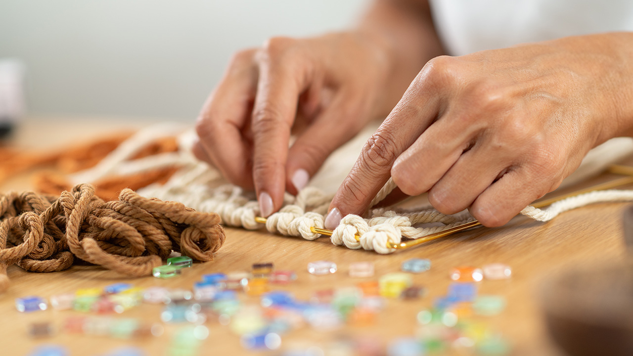 Woman crafting tapestry pattern by weaving coloured yarn strands
